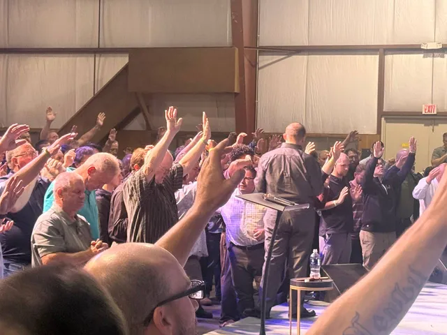 Men gathered at the front of the camp stage with hands raised in prayer.