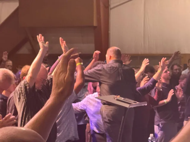 Close view from the stage as men reach forward with raised hands during prayer.