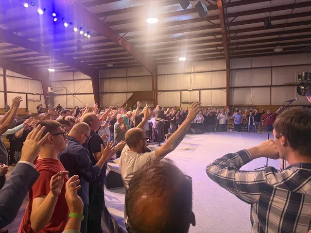 Wide view of men surrounding the open floor with hands raised in worship.