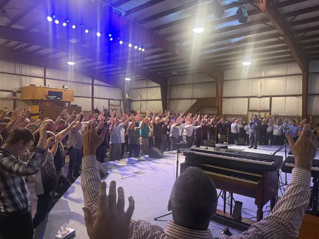 Congregation gathered in worship with raised hands across the hall.