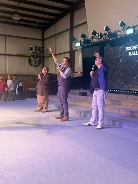 Three platform leaders with microphones during the service.