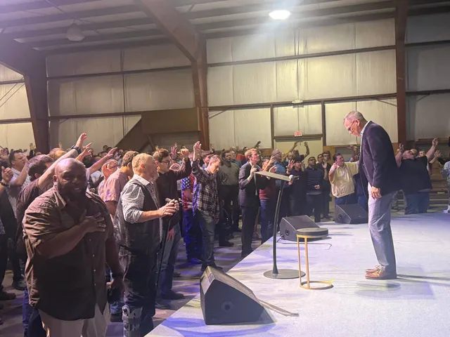 Speaker bows toward men gathered closely at the stage.