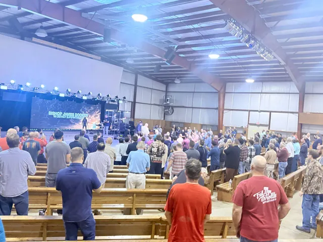 Full camp hall with men standing toward the stage under blue lighting.