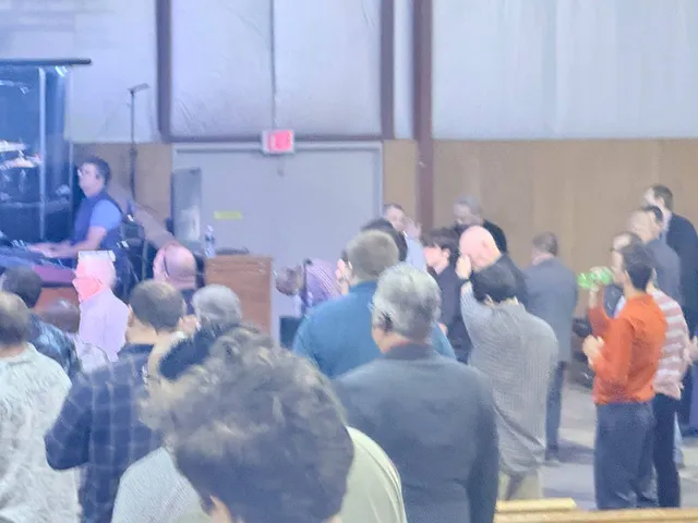 Candid soft-focus view of men standing and worshiping near the platform.