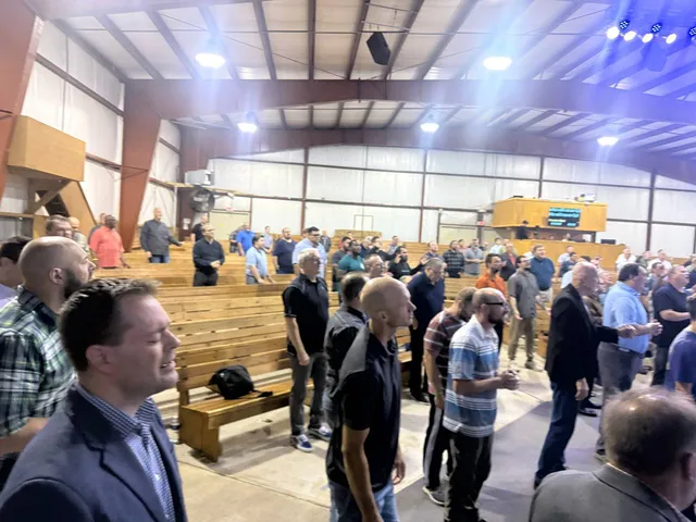 Men moving and visiting among the wooden benches after a service moment.