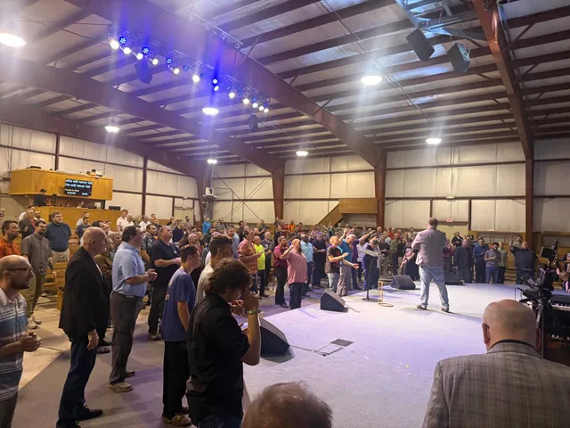Side-stage view of men gathered around the platform in prayer.