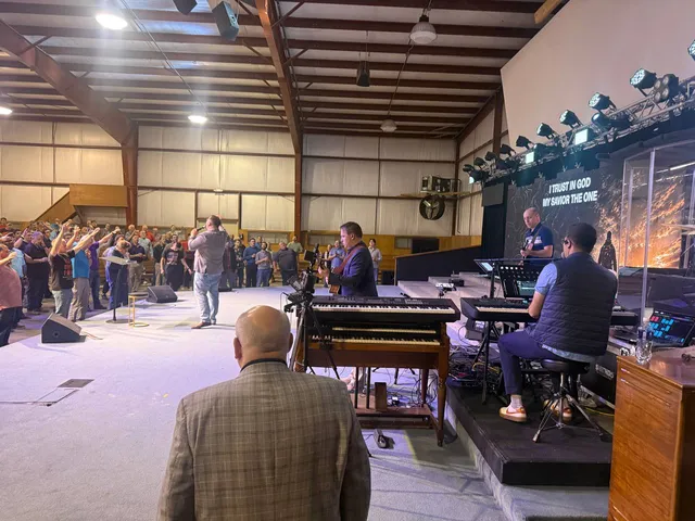 Side-stage view of worship leaders, musicians, and men with raised hands.